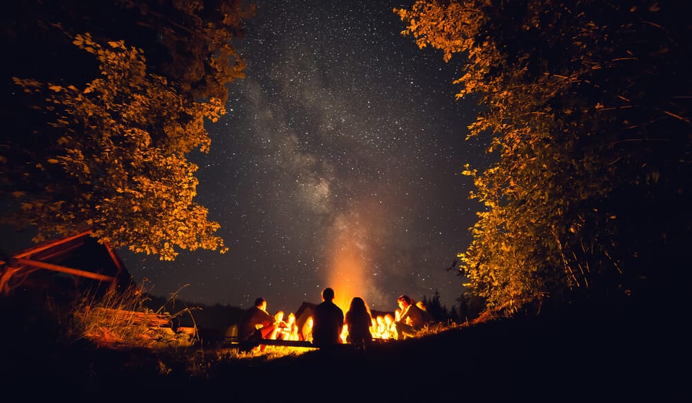 family gathered outdoors next to a fire under a starry sky