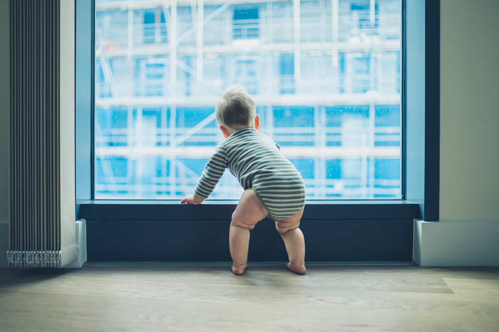 baby near a floor to ceiling window overlooking the city in small space apartment