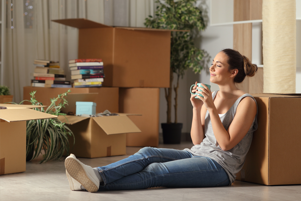 woman sitting against packed boxes enjoying a cup of coffee