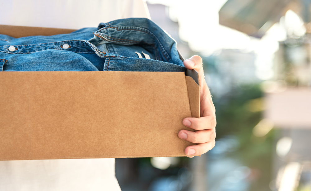 Man holding cardboard box with used clothes inside. Concept donation and reuse or recycle your used clothes