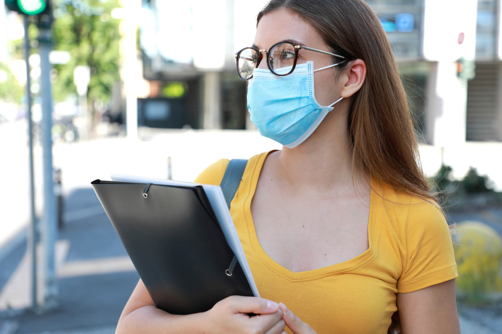 Student in Surgical Mask Walking in City Street. College Girl Back to School after Pandemic Coronavirus Disease 2019.